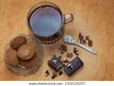 top view, on a wooden surface is tea, a vase with cookies, walnuts, chocolate waffles and a white teaspoon lies next