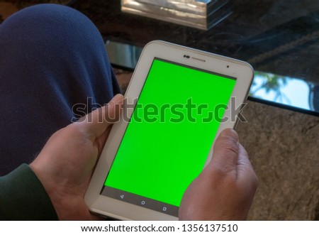 Man at Home in a living room using white tablet with Green Mock-up Screen,  Over the Shoulder Camera Shot.
