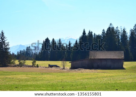 Panoramic photo of the bavarian mountains behind a hut in spring.