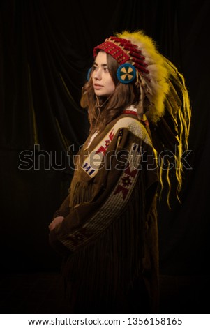The girl in clothes and a headdress of native americans in yellow light against a dark background