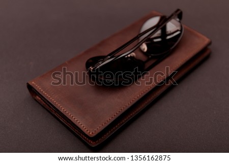 Stylish handmade brown leather wallet and black sunglass on gray background. 