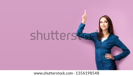 Happy smiling looking up young woman in casual blue clothing, showing something or copy space for some text or slogan, over pink background