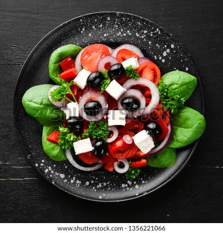 Greek salad with tomatoes, paprika, onions and feta cheese. In a black plate on a wooden background Top view. Free space for your text. Flat lay