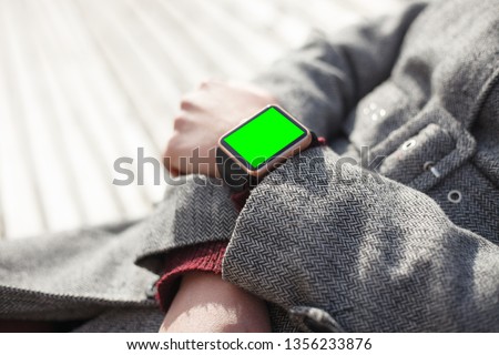 Young woman wearing modern smart watches with empty green touchscreen outdoor.White female model uses smartwatch device with chromakey screen.Place mobile application logo and text