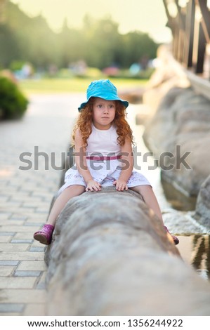Funny little red-haired girl sitting on the rocks.