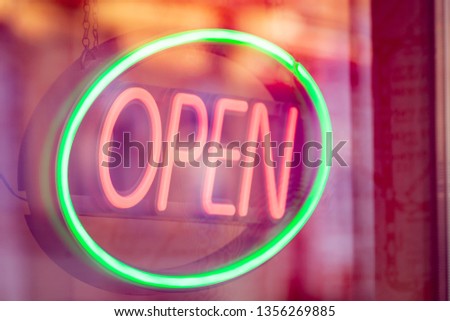 Informative colored neon open sign with red letters in a green oval in a window store, with some reflections from the street