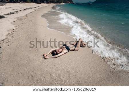 Relaxed girl enjoying tropical beach . Beautiful Brunette  in a black fashion swimsuit sunbathing on a beach. Phuket. Thailand.
