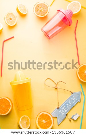 Orange and lemon juice maker, fresh summer juice, cut lemon and orange fruit with red and yellow juice container and squeezer, colored drinking straw and beach sign, on a yellow board