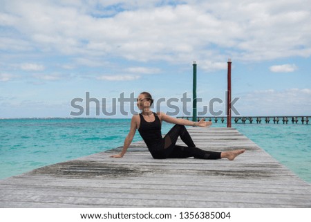 Slim fit woman in a black clothes making stretching at the pier. Turquoise water at the background. Landscape view picture. Woman making exercises at the sea.