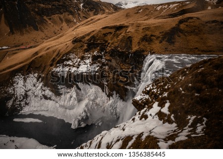 beautiful view of a waterfall and birds flying around the mountains in Iceland with snow covering the side of the mountain 