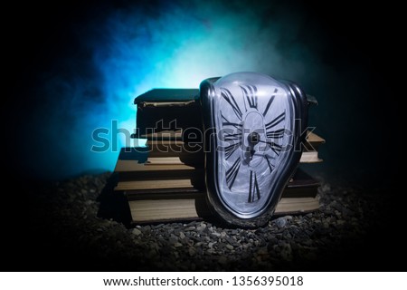 Time Concept. Distorted soft melting clock on the old books. With dark toned foggy background. Selective focus