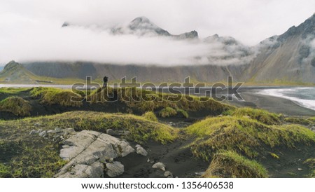 Photographer with camera and tripod taking photo of Vesturhorn Mountain in summer morning. Stokksnes, Iceland. Scenic beautiful nature landscape.  Mountains landscape. Popular tourist attraction.