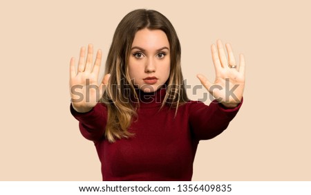 Teenager girl with turtleneck making stop gesture and disappointed over isolated ocher background