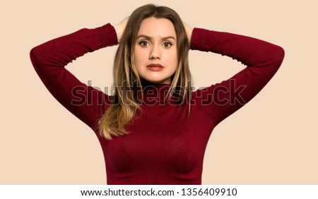 Teenager girl with turtleneck frustrated and takes hands on head over isolated ocher background