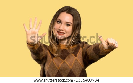 Teenager girl with brown sweater counting six with fingers over isolated yellow background