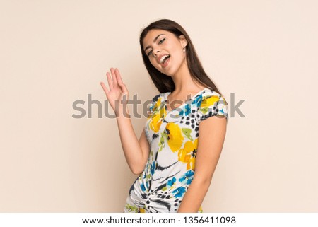 Teenager girl with floral dress saluting with hand with happy expression