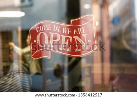 Business vintage sign that says Come in We're Open on barber and hair salon shop window - Image of abstract blur barbershop with people in the background bokeh