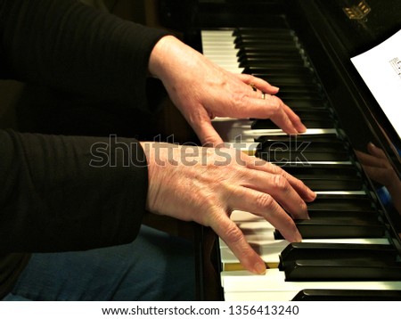 Senior woman playing piano. Close up side view of elderly hands and fingers playing a song on the keys of an upright shiny black piano.