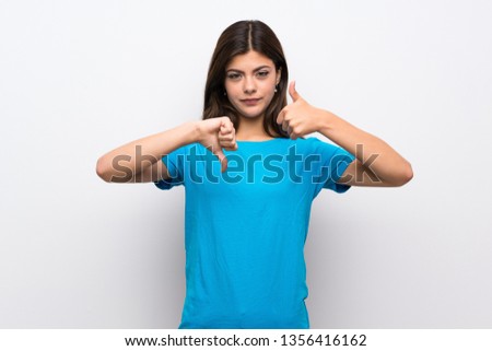 Teenager girl with blue shirt making good-bad sign. Undecided between yes or not