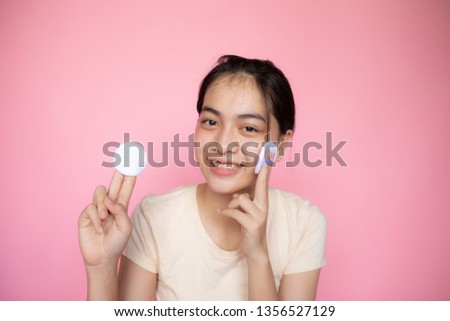 Young cute teenager Asian holding makeup sponge pad and smile in font of the pink isolated background