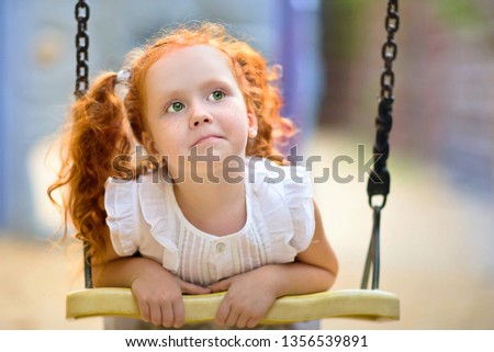 Portrait of a little red-haired girl on a swing.