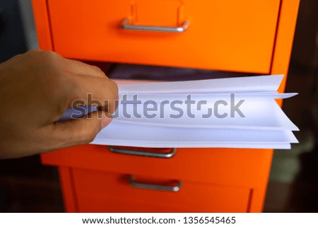 Woman's hand pick up white papers for write letter, Filing cabinet with open drawer, Orange metal colour, Administration and storage concept, closeup & Macro shot, Selective focus