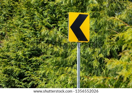 Left turn arrow sign along a bend in a road, with an evergreen tree background in a transportation concept