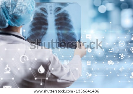 A young doctor is standing backside and examining the lungs image with total medical system structure at the foreground. The concept of medical service, diagnosis and treatment.