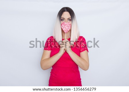 Photo of happy woman wearing dress eating big heart candy isolated over white background