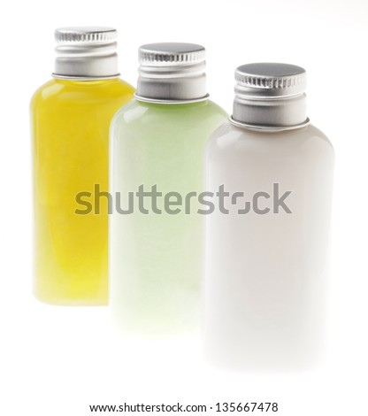 Three small transparent plastic bottles filled with green, pastel green and white cosmetic lotions/creams and sealed with silver metal caps. The contents of the bottle can be lotion, shampoo, etc.