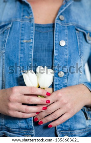 Fragment of a girl dressed in denim. In the hands of holds three white Tulip
