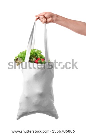 Female hand holding eco bag with products on white background