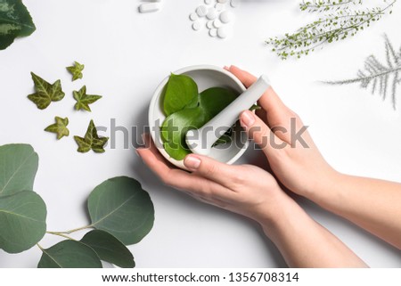 Female hands with mortar, different herbs and plant based pills on white background Royalty-Free Stock Photo #1356708314