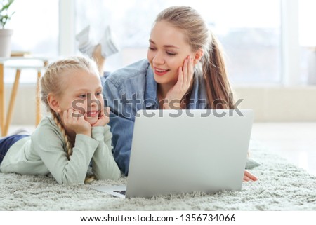 Young mother with little daughter watching cartoons at home