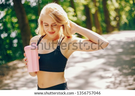 Stylish girl in a sportwear. Cute woman standing in a sunny park. Lady with bootle of water