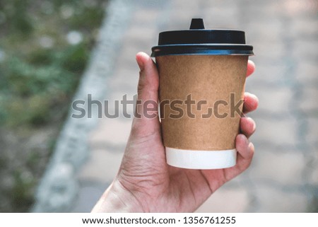 Coffee paper crafting cup holds female hand on a blurred background. Place for text or logo.