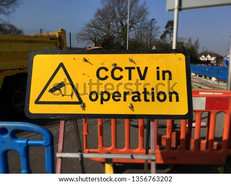 CCTV in operation warning sign on road repair work site. The portable metal sign is surrounded by safety barrier around work area.