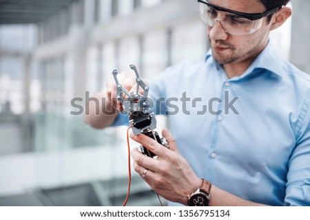 A young businessman or scientist with robotic hand standing in office, working. Royalty-Free Stock Photo #1356795134