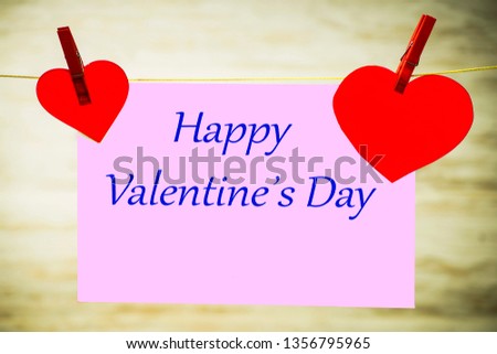 A card and two red hearts hanging on a string, fastened with red buckles with the words Happy Valentine's Day