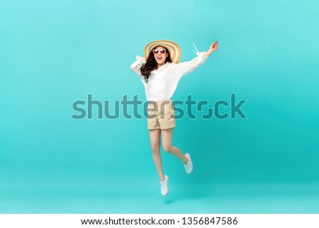 Studio shot of happy energetic asian woman wearing summer fashion attire jumping in mid-air motion isolated in light blue background