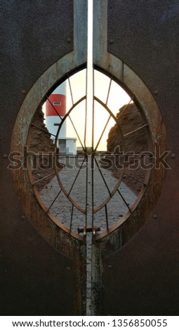 Sunset on the ocean, red and white lighthouse and stone pavement behind a wooden door with an oval window