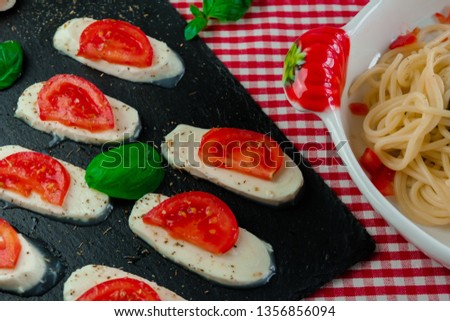 Spaghetti with pesto sauce, mozzarella with tomato and basil, served on checkered tablecloth. Close-up