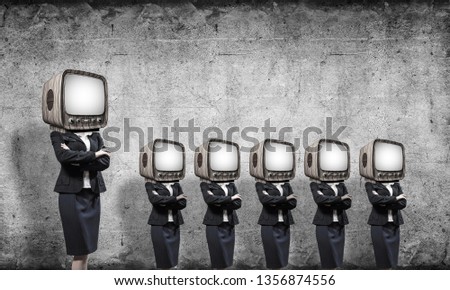 Business women in suits with old TV instead of their heads keeping arms crossed while standing in a row in empty room with gray wall on background.