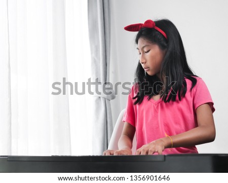 Asian girl playing keyboard piano near window at home.