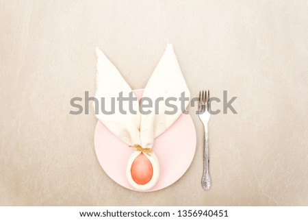 Easter bunny (rabbit) egg concept, table arrangement decoration. Pink (rosy) eggs with plate, fork, cloth vintage linen napkin on a stone background, top view.