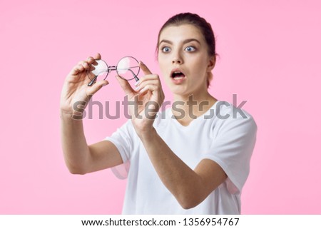 Surprised woman in a white T-shirt holding round glasses in her hands on a pink background