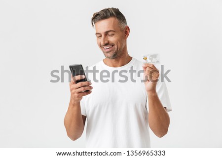 Image of happy man 30s wearing casual t-shirt holding smartphone and plastic credit card isolated over white background