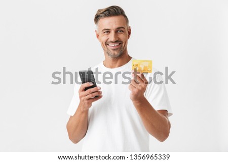 Image of smiling man 30s wearing casual t-shirt holding smartphone and plastic credit card isolated over white background