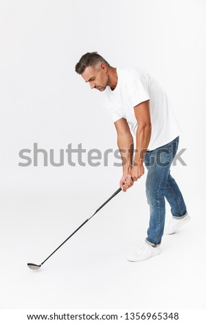 Full length image of masculine man 30s wearing casual t-shirt holding club and playing golf isolated over white background