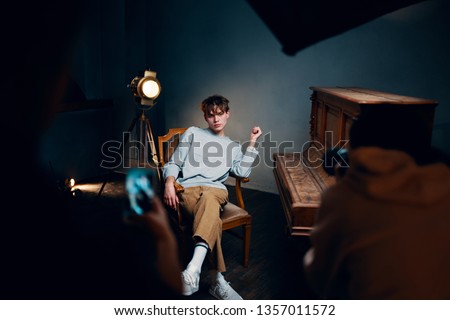 cute elegant man sitting next to piano chairs floodlight photo shoot